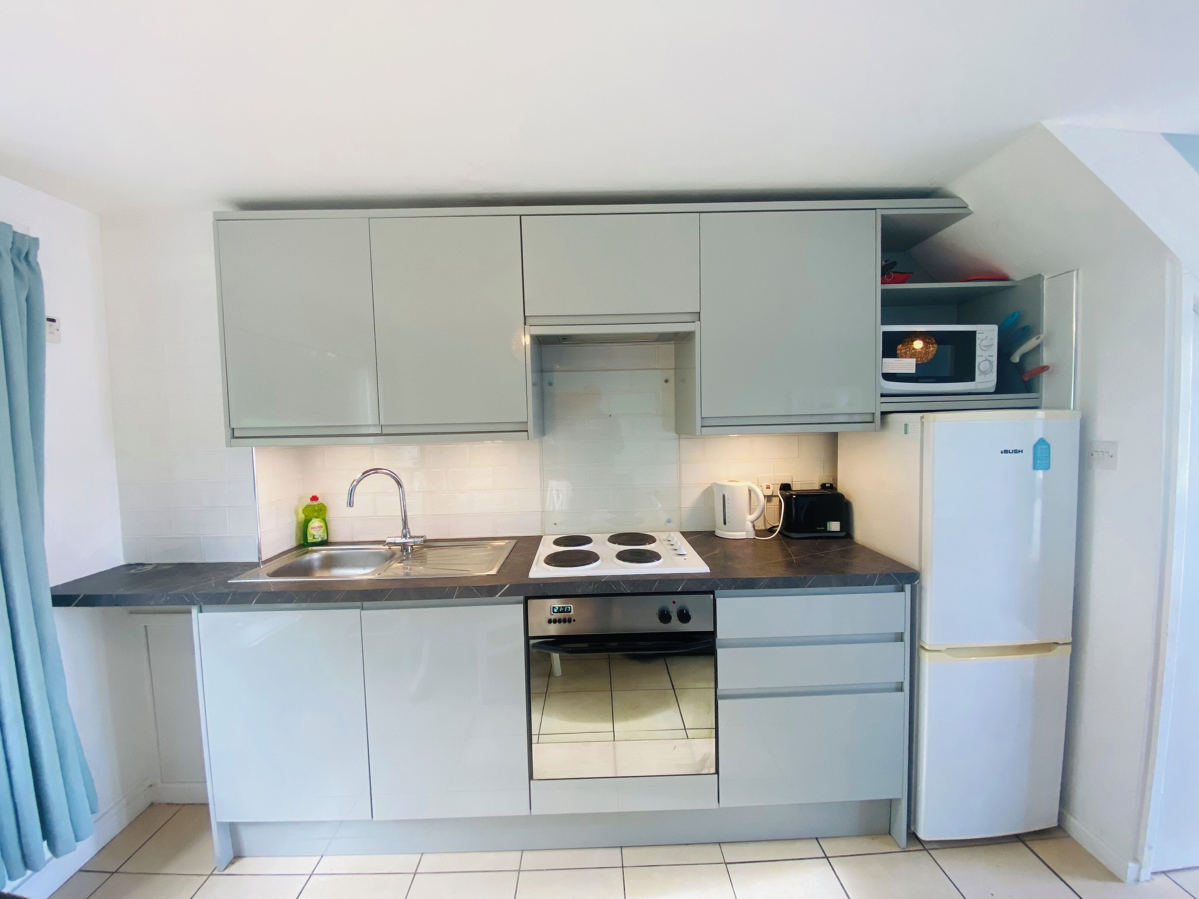Cocina pequeña equipada con lavaplatos, estufa, microondas y refrigerador.