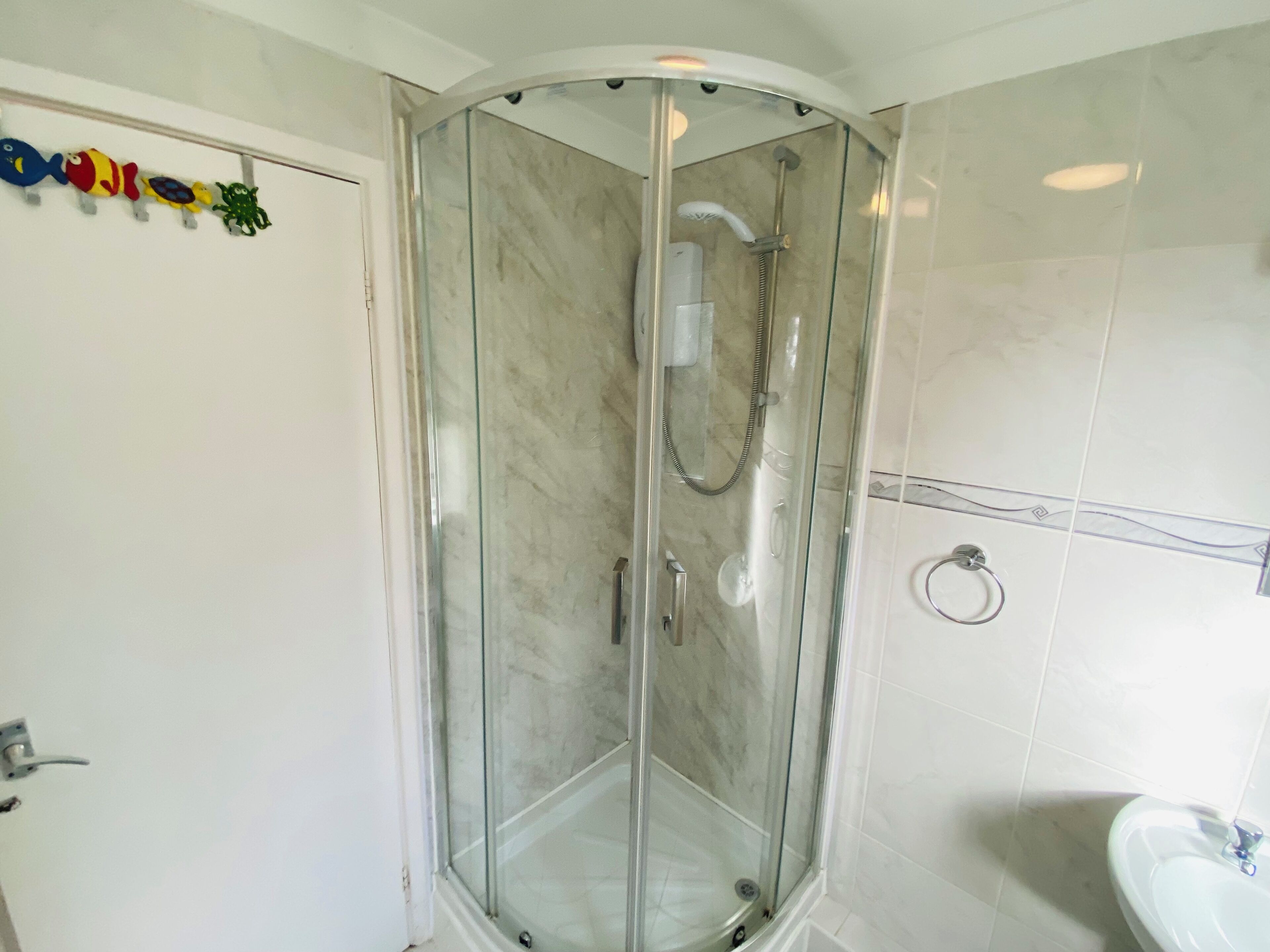Eine begehbare Glasdusche mit Duschbrause, einem Händetuchhalter an der Wand und einem Waschbecken mit Spiegel.