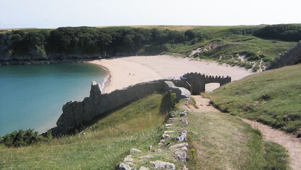 Un paisaje costero con una playa de arena, un camino de piedra y un puente de piedra que conduce a la playa.