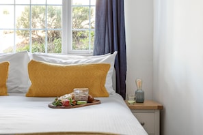 A neatly made bed with yellow patterned pillows, a tray of fresh fruit, and a glass of water on a bedside table.