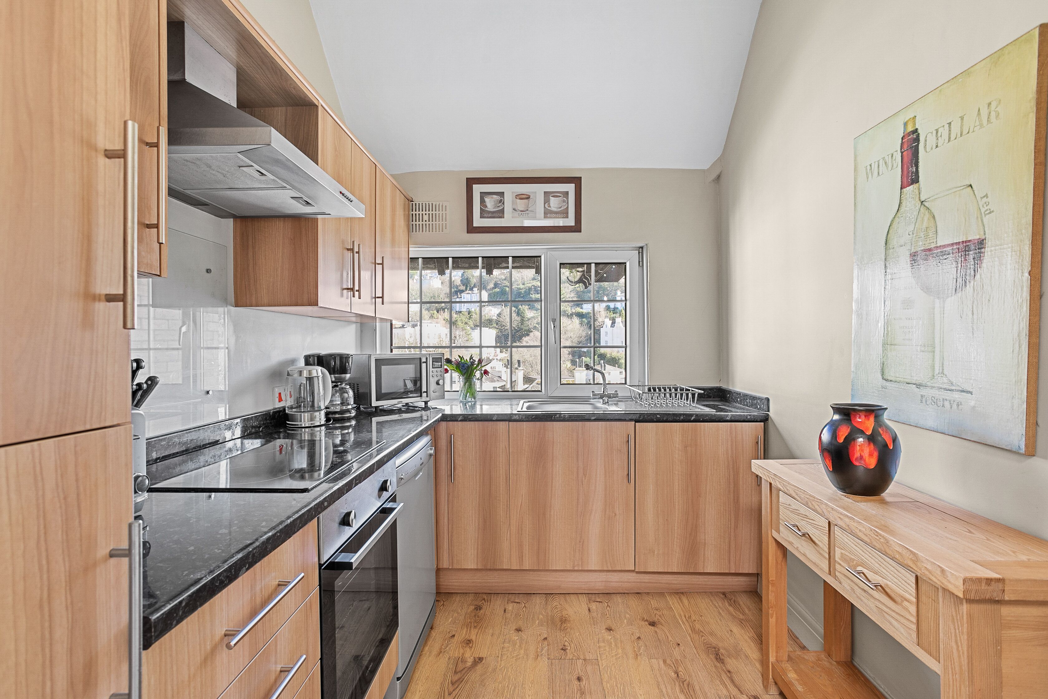A modern kitchen with wooden cabinets, a black countertop, and a large window providing natural light.