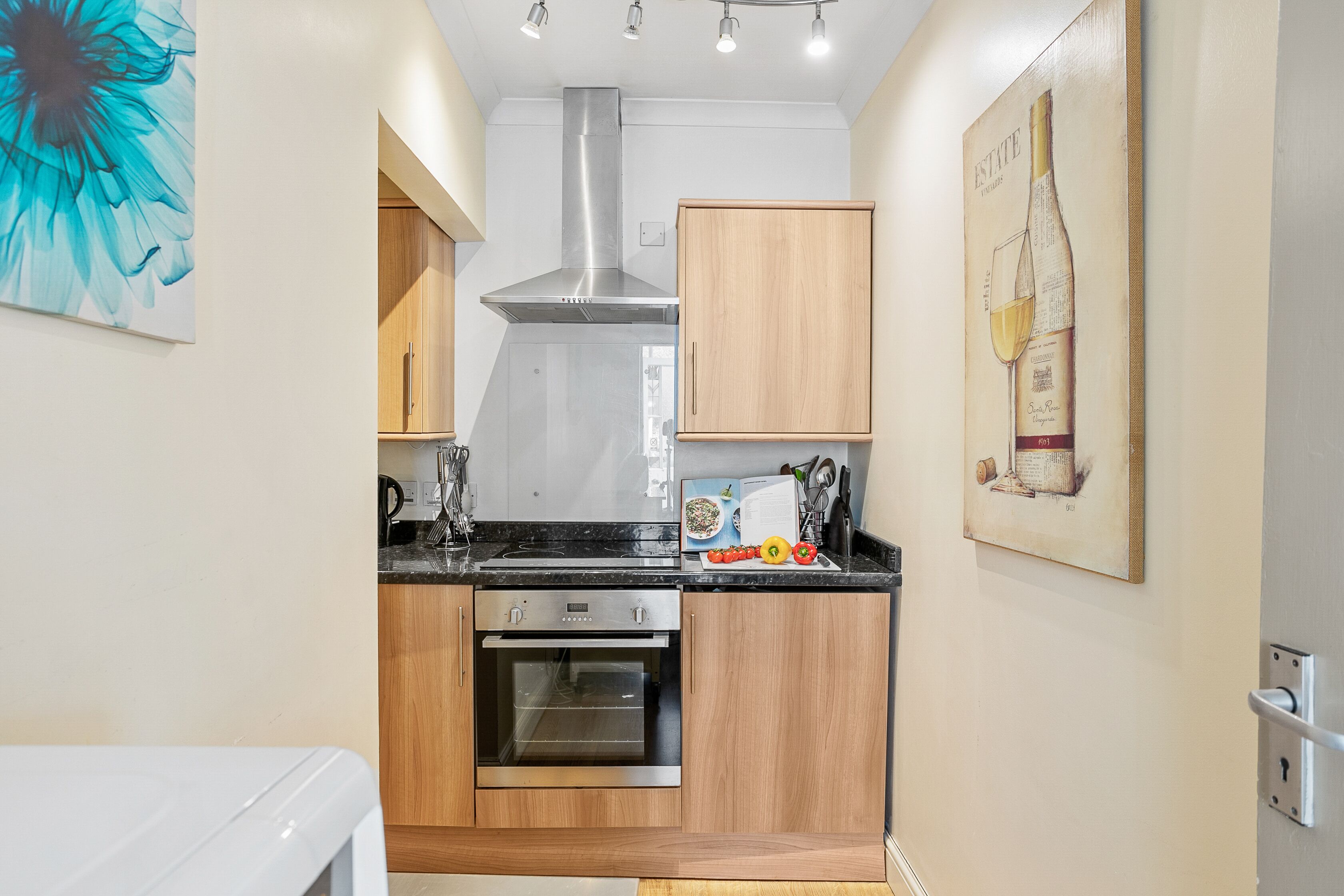 A compact kitchen with wooden cabinets, a stainless steel range hood, and a built-in oven.