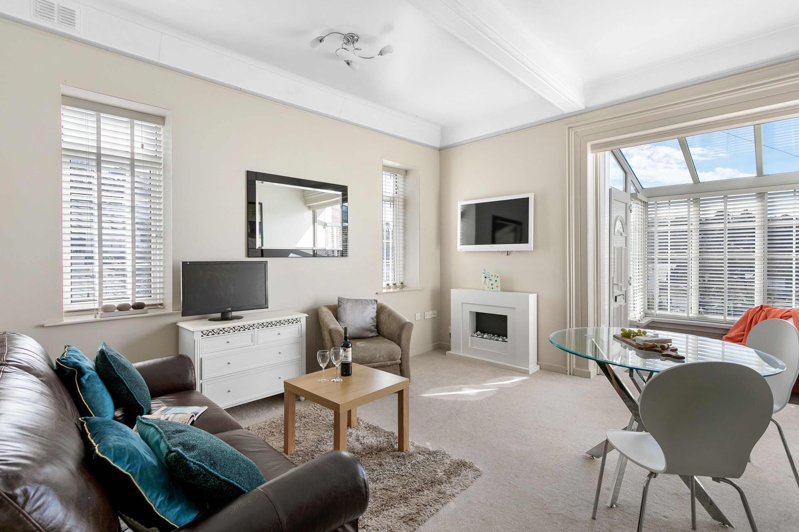 A modern living room with a leather sofa, a glass coffee table, and a fireplace.
