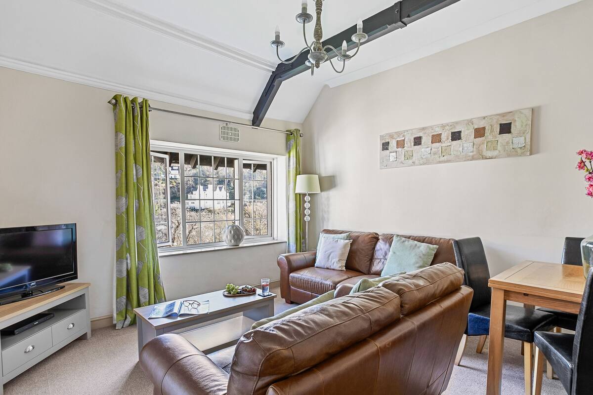 Ein Wohnzimmer mit Fernseher, Sofa, Couchtisch und Esstisch mit Stühlen.