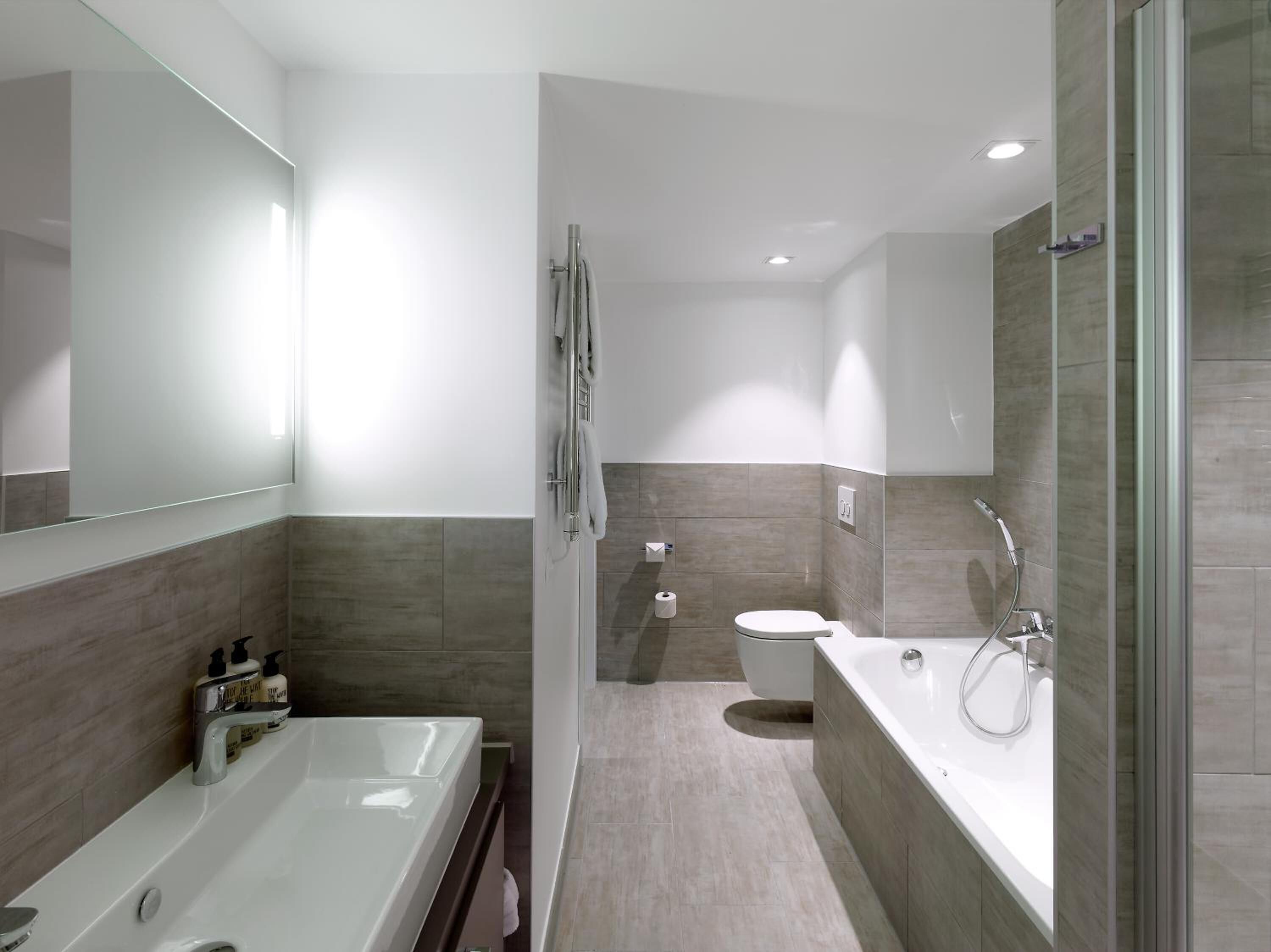 A modern bathroom with a bathtub, a large mirror, a toilet, and a shower area.