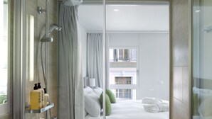A modern bathroom with a glass shower enclosure, a bathtub, and a bed with white linens and pillows.