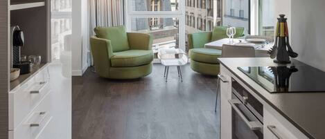 A modern kitchen with white cabinets, a dining area with a green sofa, and a view of the city through large windows.