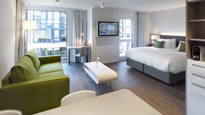 A modern hotel room with a bed, a desk, a green sofa, and a television. - Base Nyon (Nyon)