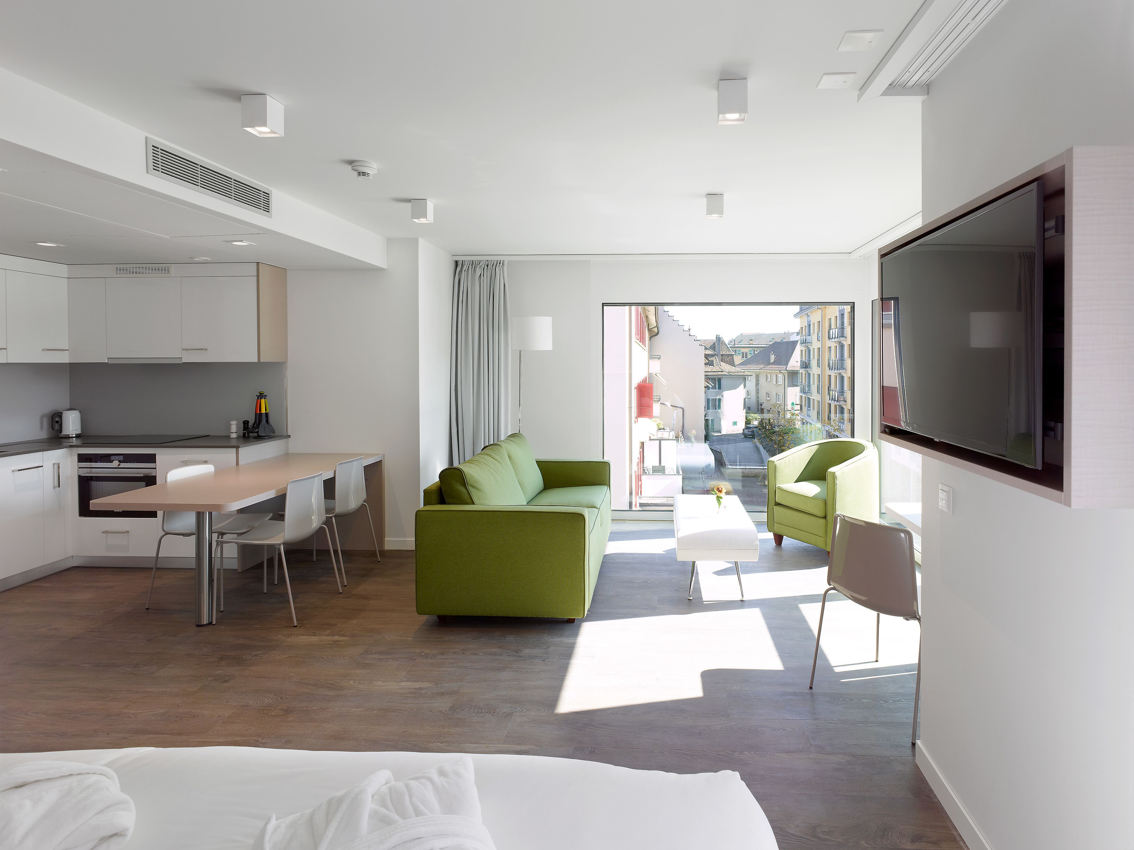 Ein modernes Hotelzimmer mit Küchenzeile, einem grünen Sofa, einem Fernseher und einem Balkon mit Blick auf die Stadt.