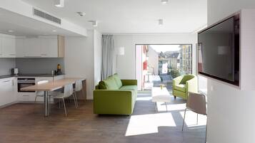 Ein modernes Hotelzimmer mit Küchenzeile, einem grünen Sofa, einem Fernseher und einem Balkon mit Blick auf die Stadt.