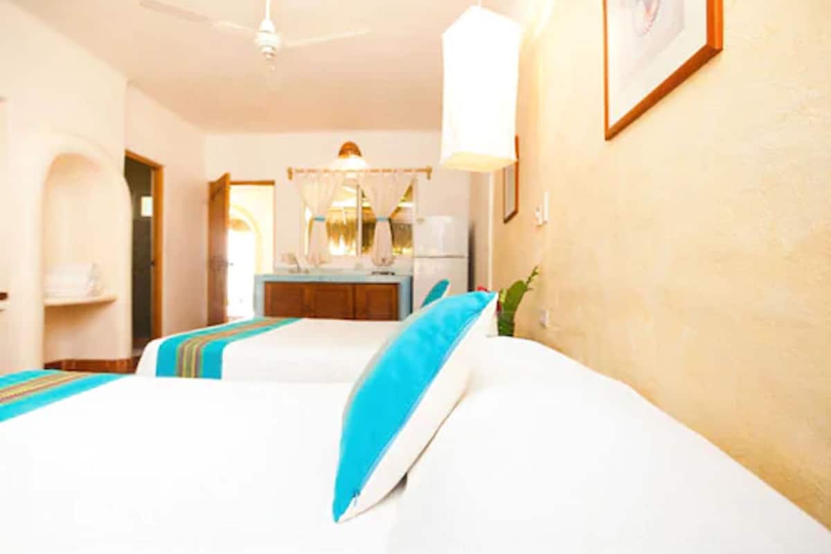 Une chambre d’hôtel avec deux lits, un bureau et un ventilateur de plafond.