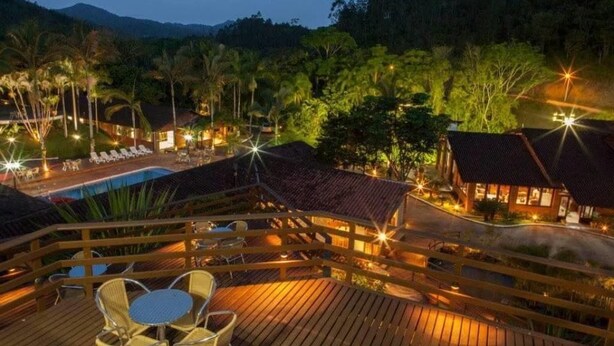 A resort with a wooden deck, lounge chairs, a swimming pool, and a mountain backdrop. - Pousada Arraial do Ouro (Gaspar)