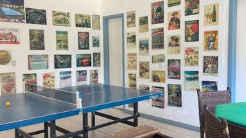 Quarto com mesa de futebol de mesa, mesa de pingue-pongue e parede decorada com cartazes antigos.