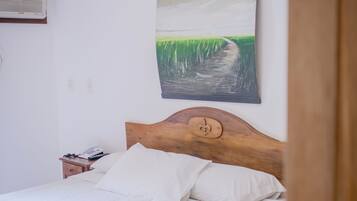 Una cama bien hecha con sábanas blancas, un cabecero de madera y un cuadro de un paisaje sobre ella.