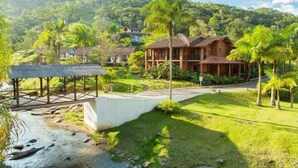 A resort with a wooden house, a bridge, and lush greenery. - Pousada Arraial do Ouro (Gaspar)