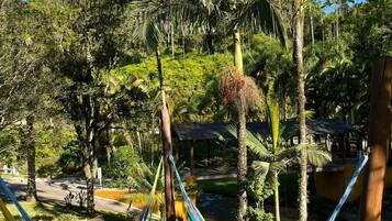 A hammock in a lush garden with palm trees and a small building in the background.