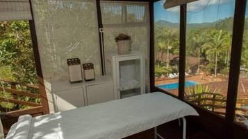 Quarto com cama, um armário pequeno branco e janela com vista para uma piscina e vegetação.