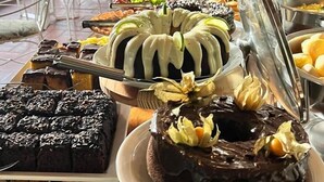 A buffet with various desserts including cakes and pastries, arranged on a table with a view of outdoor seating. - Pousada Arraial do Ouro (Gaspar)