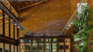 A rustic interior with exposed brick walls, a wooden ceiling, and a large window with a view of greenery. - Pousada Arraial do Ouro (Gaspar)