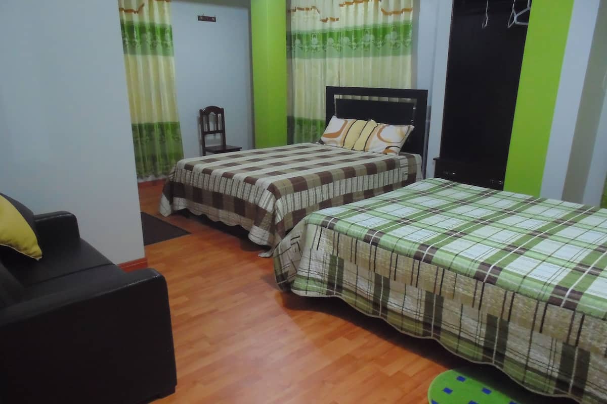 A bedroom with two beds, a wooden floor, a green mat, and a black chair.
