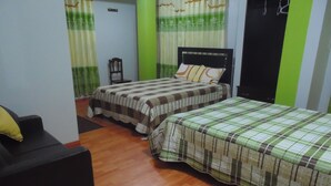 A bedroom with two beds, a wooden floor, a green mat, and a black chair.