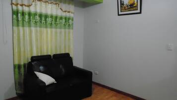 A room with a black leather sofa, a green and white striped curtain, a framed picture on the wall, and wooden flooring.