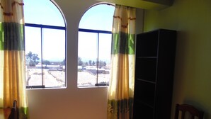A room with two large windows, a wooden chair, and a bookshelf.