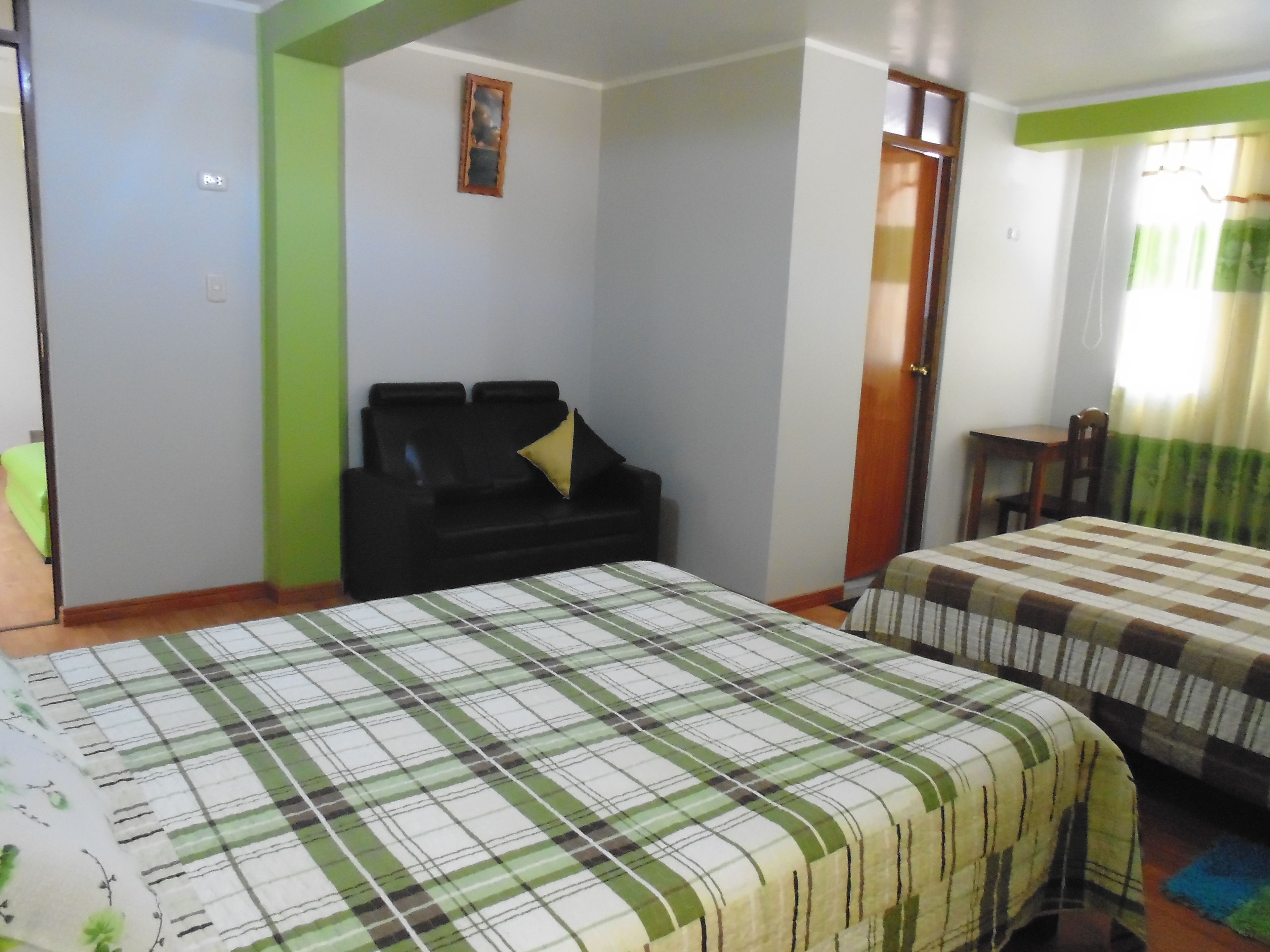Quarto de hotel com cama, sofá, uma pequena mesa e uma janela com cortinas.