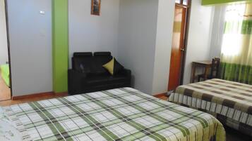 Quarto de hotel com cama, sofá, uma pequena mesa e uma janela com cortinas.
