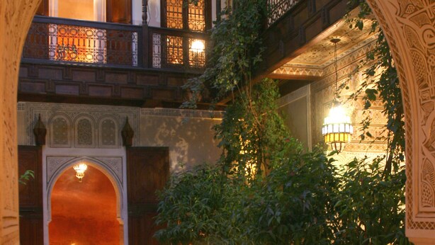 Un patio ornamentado con suelo de baldosas, una fuente central y un comedor con mesa preparada para dos.