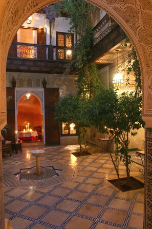 An ornate courtyard with a tiled floor, a central fountain, and a dining area with a table set for two. - Riad Samsara (Marrakech)