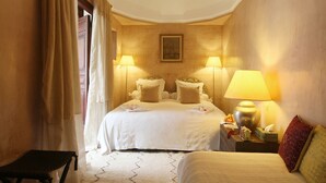 Una habitación de hotel con cama, dos lámparas de noche, mesita de noche, una silla y una ventana con cortinas.