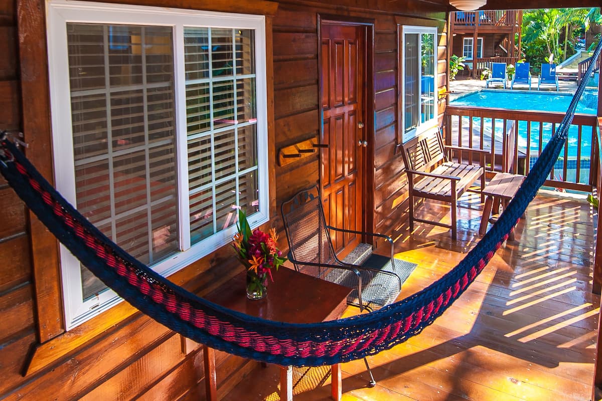 A wooden cabin with a hammock, a pool, and a patio area.