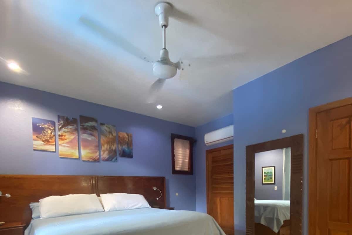 A bedroom with a wooden bed, a ceiling fan, and a blue wall with three paintings.