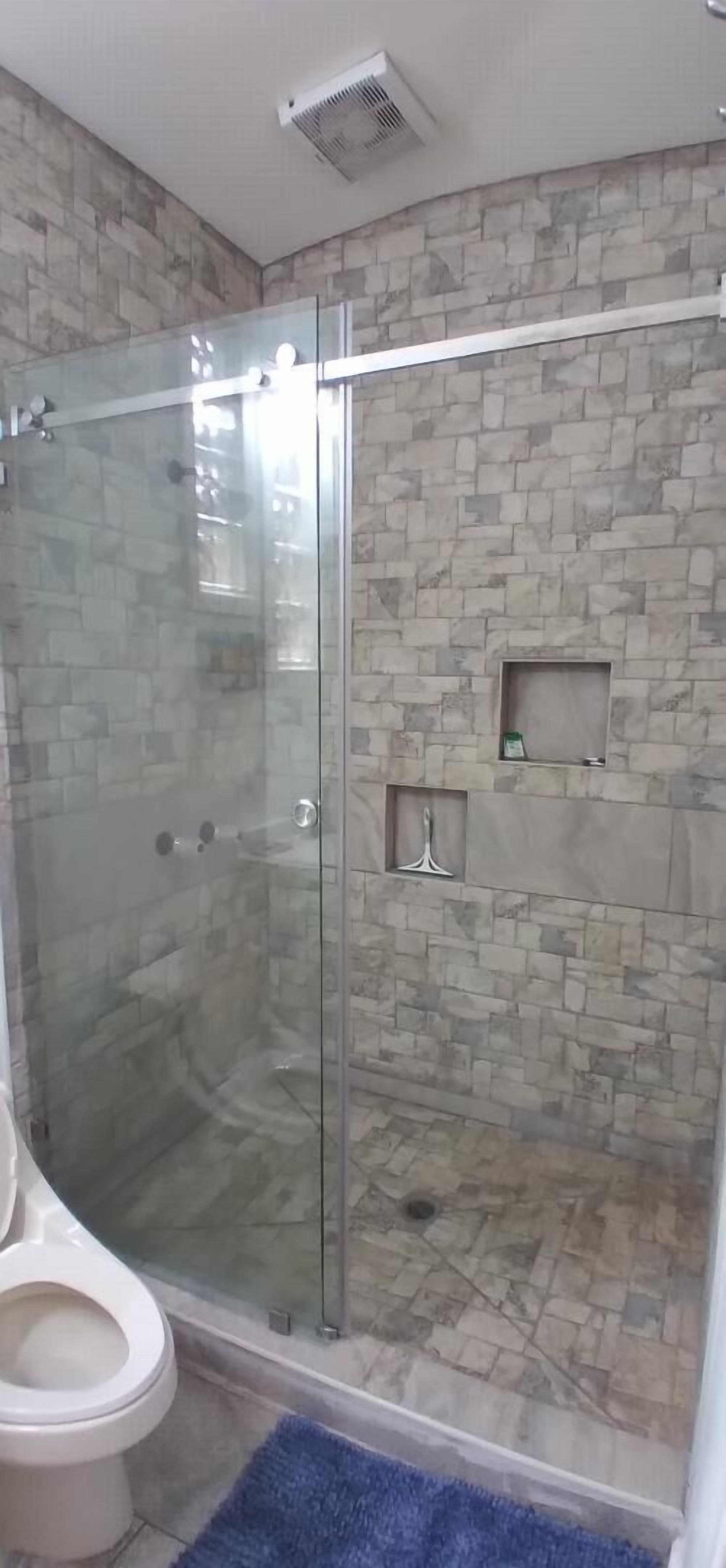 A bathroom with a glass-enclosed shower, a toilet, and stone-patterned walls.