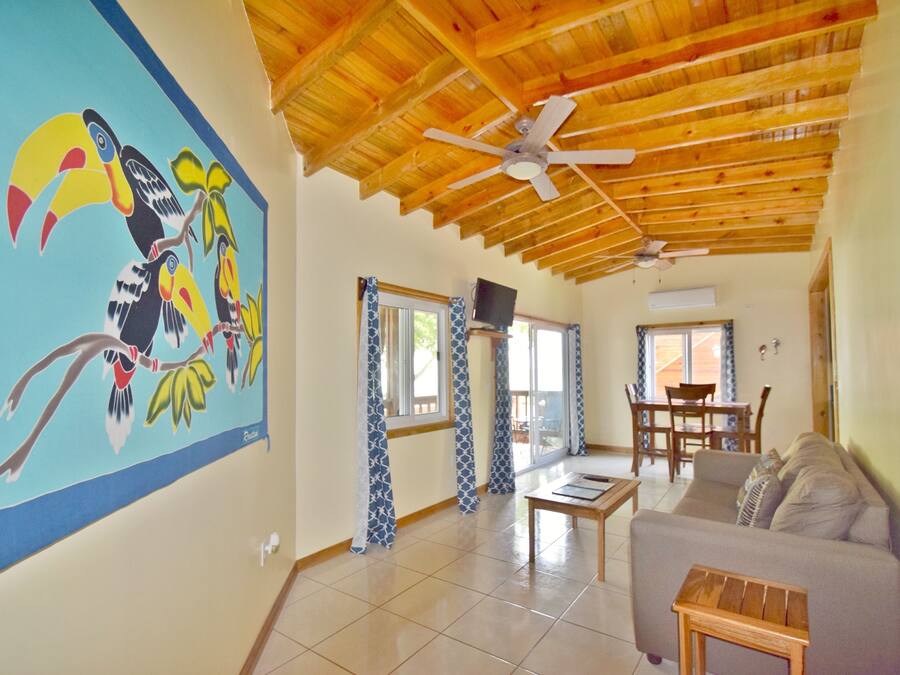 A spacious living area with a wooden ceiling, a large mural of toucans, a dining area, and a sofa.