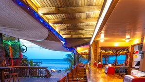 Um restaurante à beira-mar com piso de madeira, assentos vermelhos e vista para o oceano.