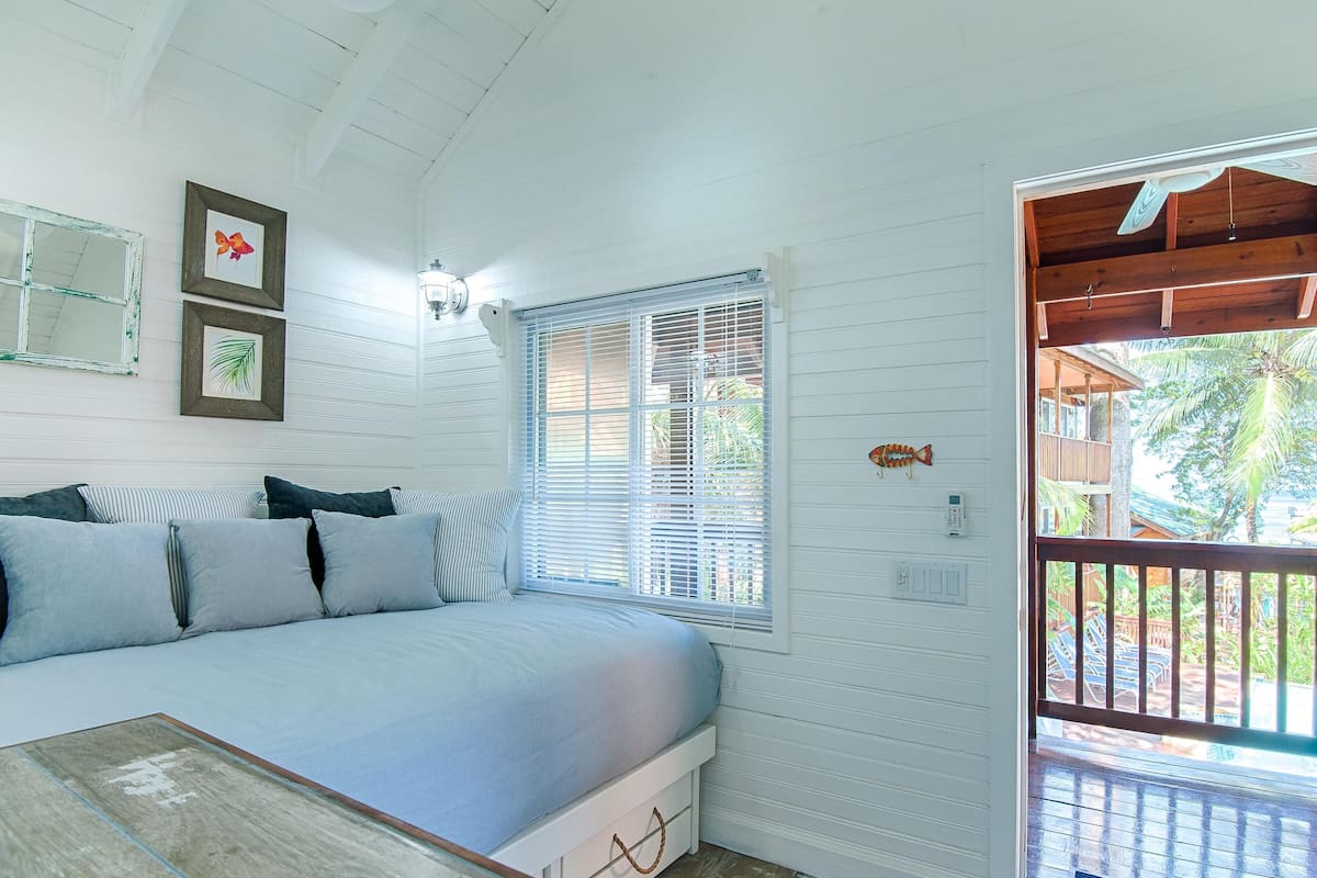 A bedroom with a bed, a window with blinds, a wall-mounted light fixture, and a door leading to an outdoor area.