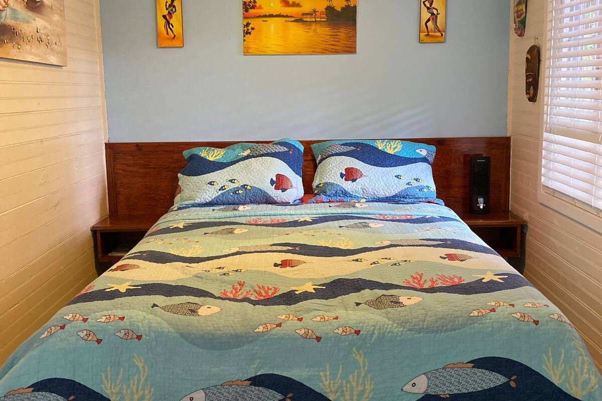 A bedroom with a bed featuring a marine-themed bedspread, a ceiling fan, and artwork on the walls.