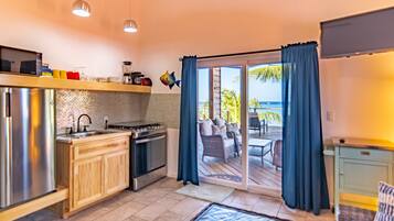 Cocina moderna con refrigerador, estufa y lavamanos de acero inoxidable. Cuenta con un comedor con mesa y sillas, y vista al océano a través de amplias puertas corredizas de vidrio.