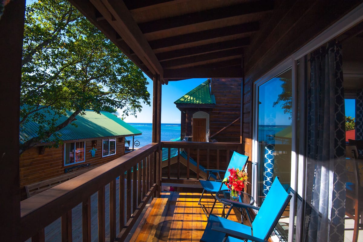 A wooden deck with a view of the ocean, a gazebo, and a chair with a vase of flowers.