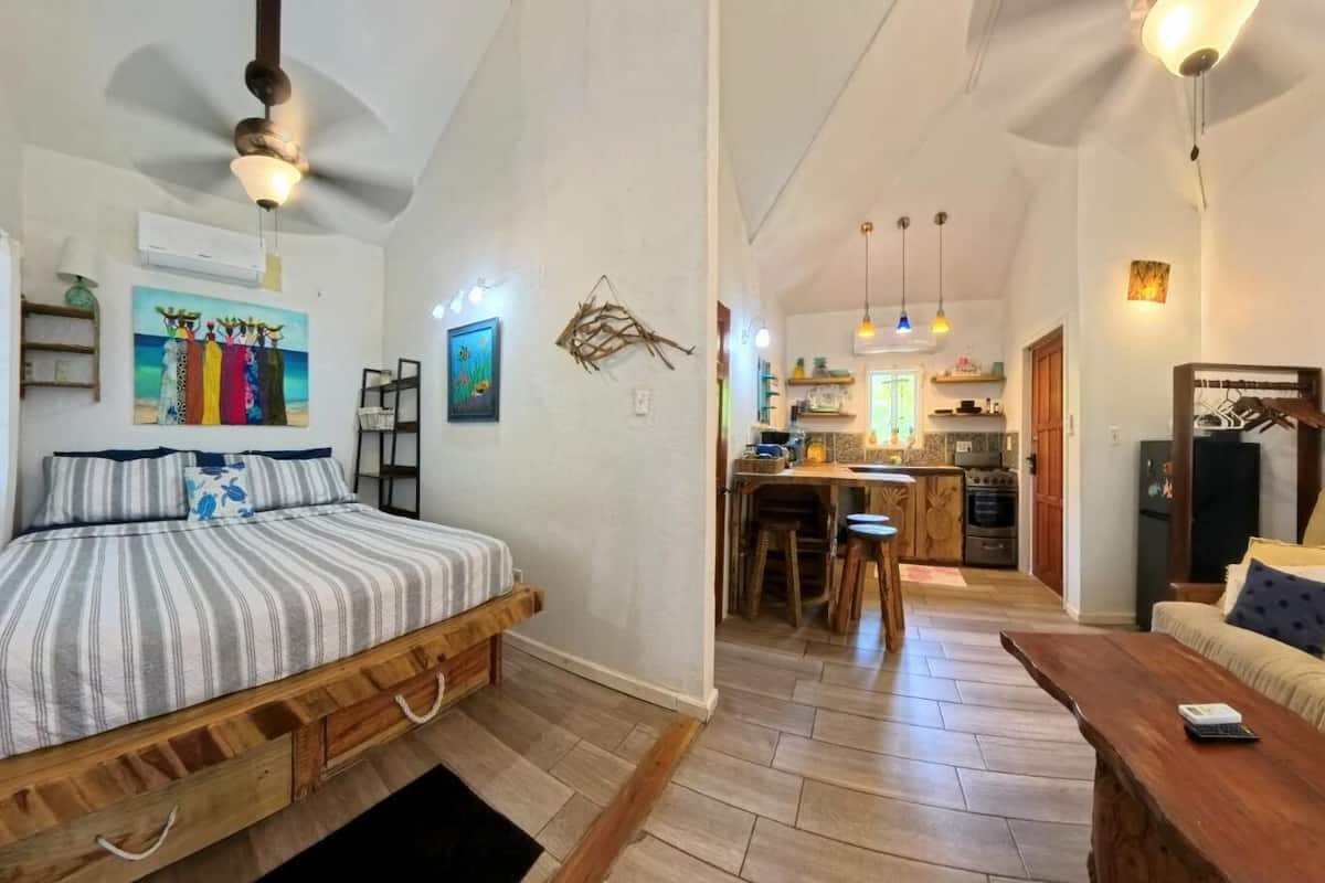 A bedroom with a bed, a wooden floor, a kitchen area with a dining table, and a living room with a sofa.