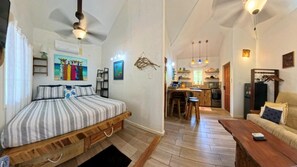 A bedroom with a bed, a wooden floor, a kitchen area with a dining table, and a living room with a sofa. - Blue Bahia Resort (Roatan)
