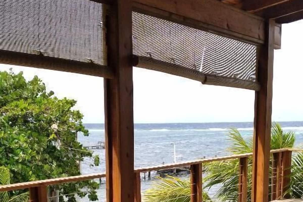 A wicker sofa with cushions on a wooden deck overlooking the ocean.