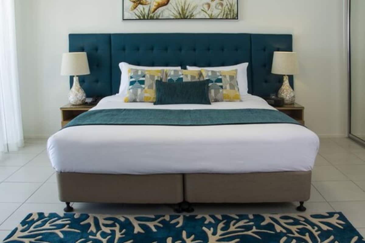 Een slaapkamer met een groot bed, een blauw hoofdeinde en een decoratief schilderij erboven.