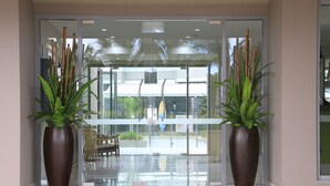 Ein Hotel Eingang mit Glastür, zwei große Kübelpflanzen, einer hölzernen Bank und einem gefliesten Boden.