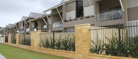 A row of modern townhouses with balconies, stone walls, and a well-maintained lawn.