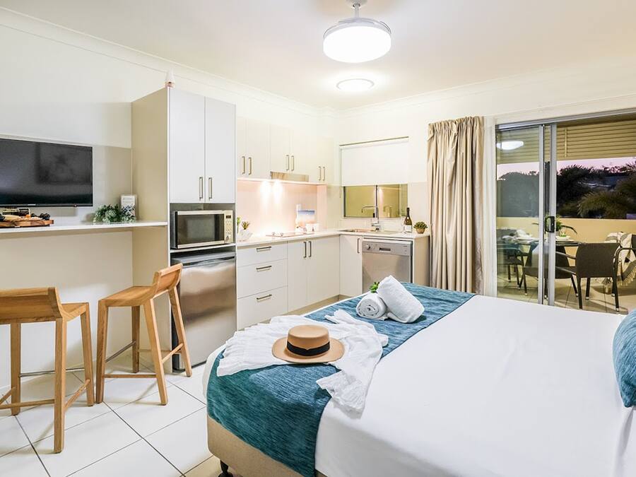 Una habitación de hotel moderna con cama, escritorio con televisor, kitchenette y balcón con vistas.