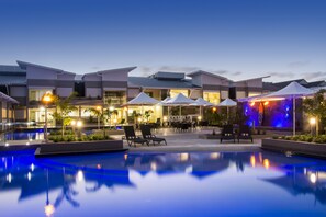 Een modern hotel met een zwembad, terras en sfeerverlichting.