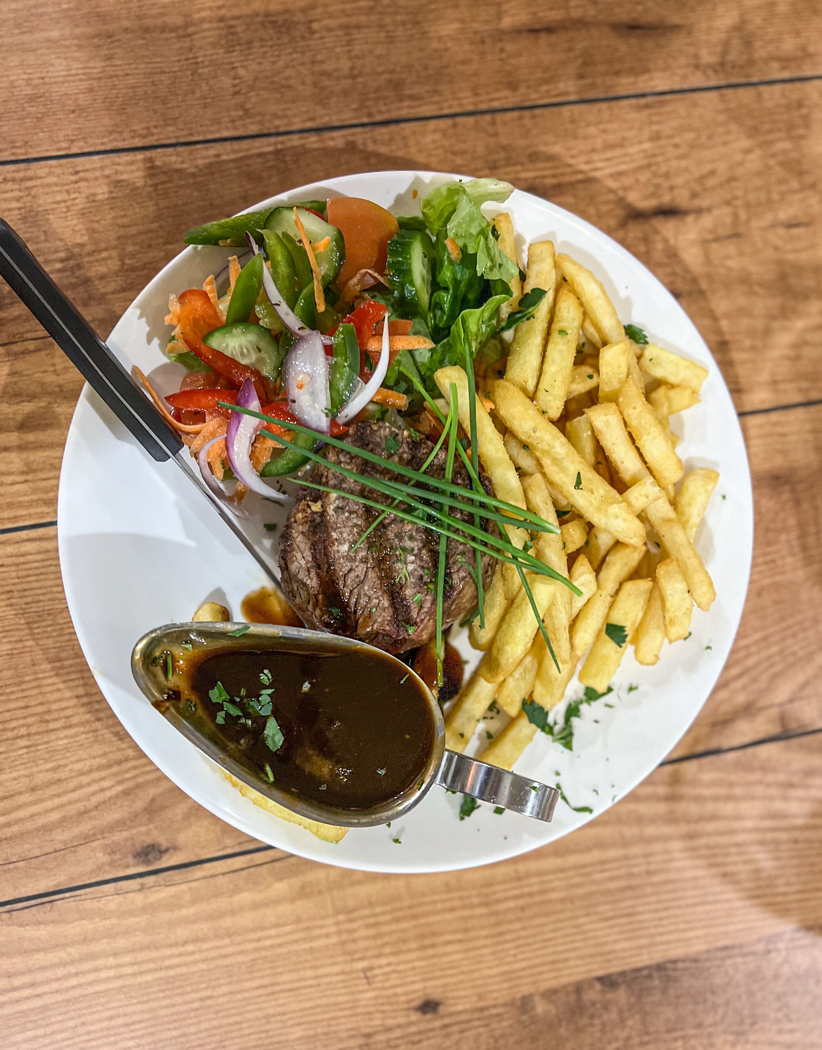 Un plato con un bistec, papas fritas y una ensalada.